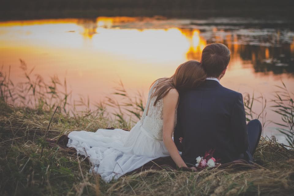 Casal de noivos sentado à beira de um lago no fim da tarde