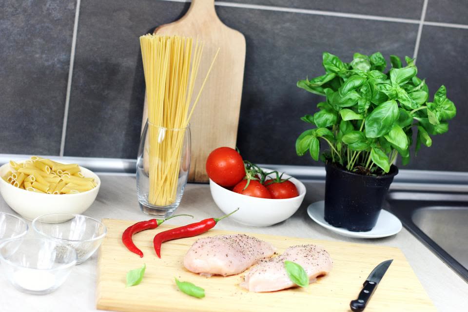Bancada de cozinha com tomates, manjericão, massa e frango
