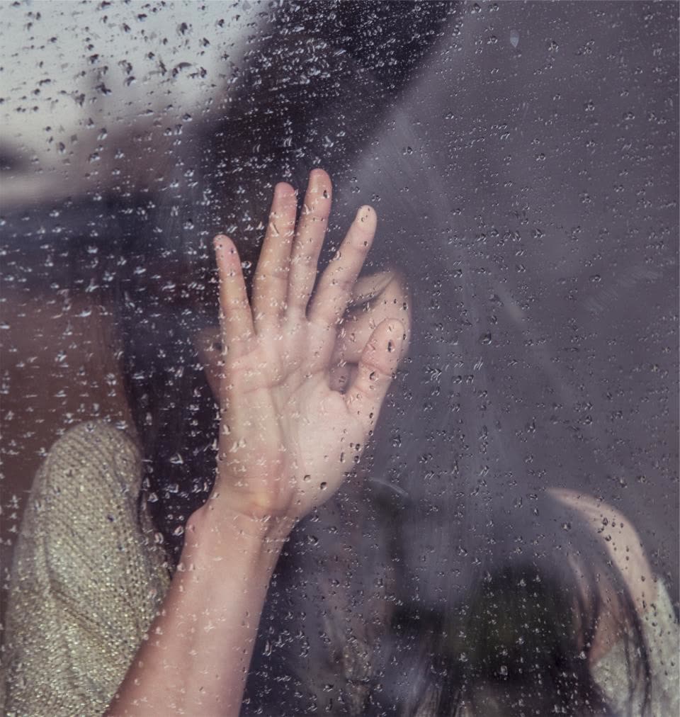 Mão apoiada em uma janela molhada de chuva